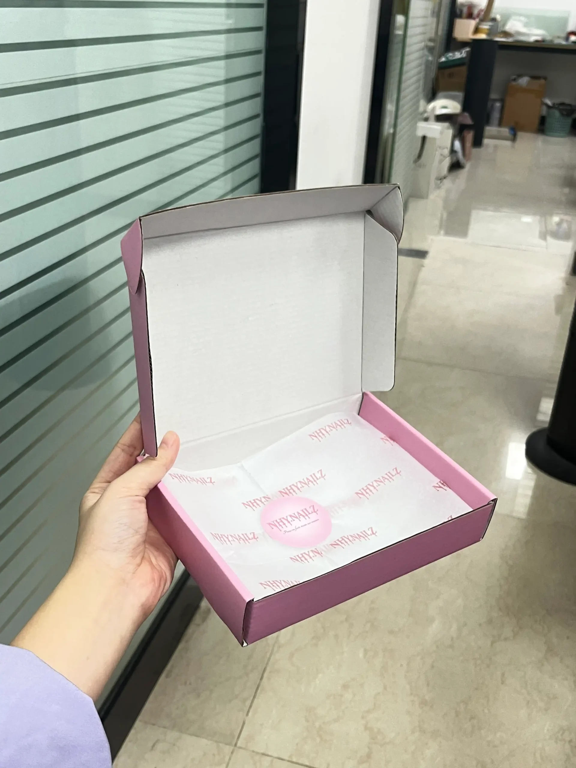 Open pink mailer box with branded tissue paper and sticker